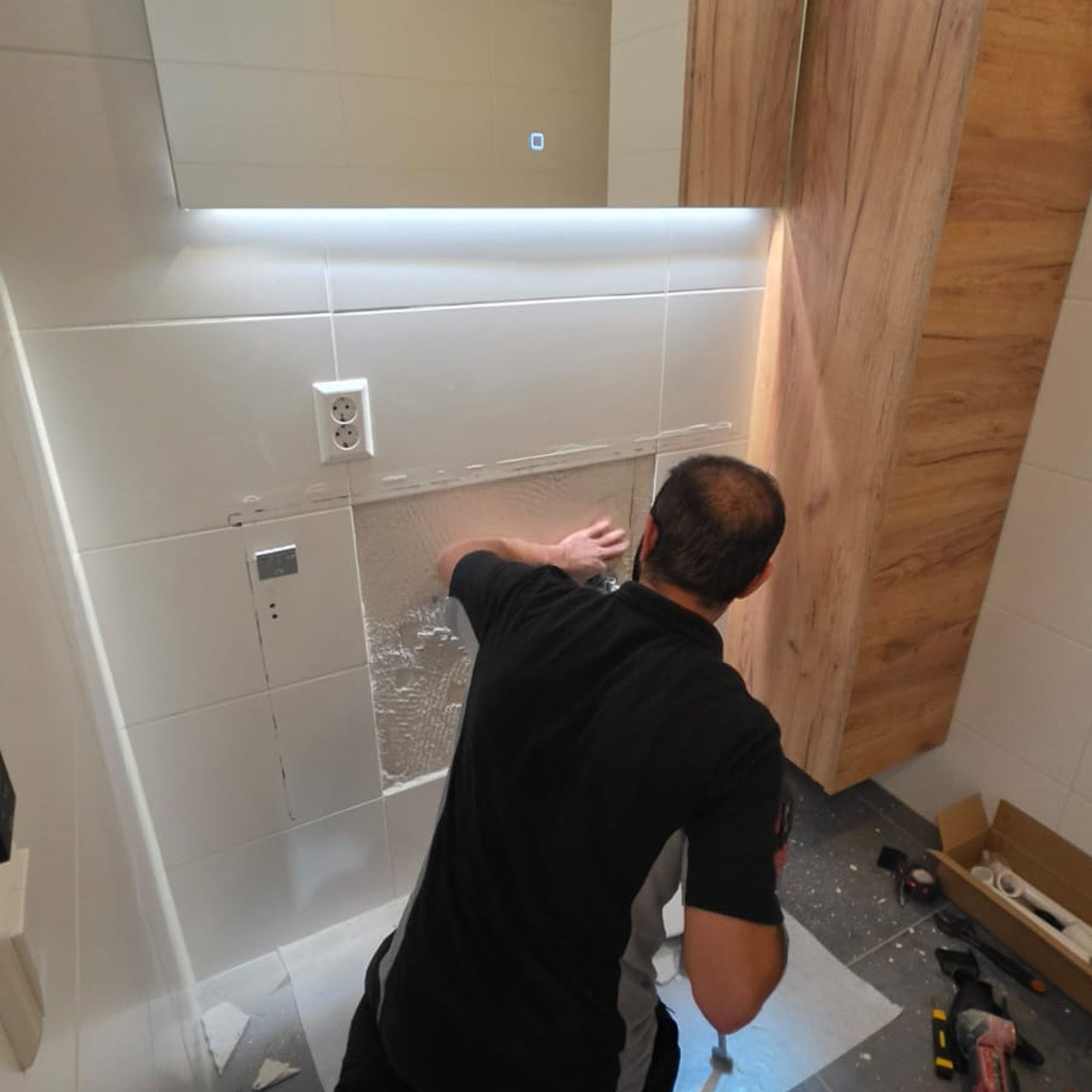 Vakman werkt aan de wand onder een verlichte badkamerspiegel