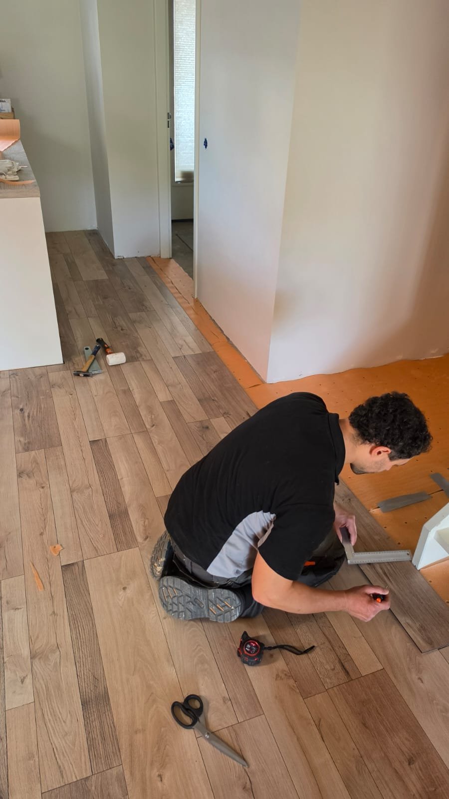Vakman meet een PVC-vloerplank op maat tijdens het leggen van een houtlook vloer