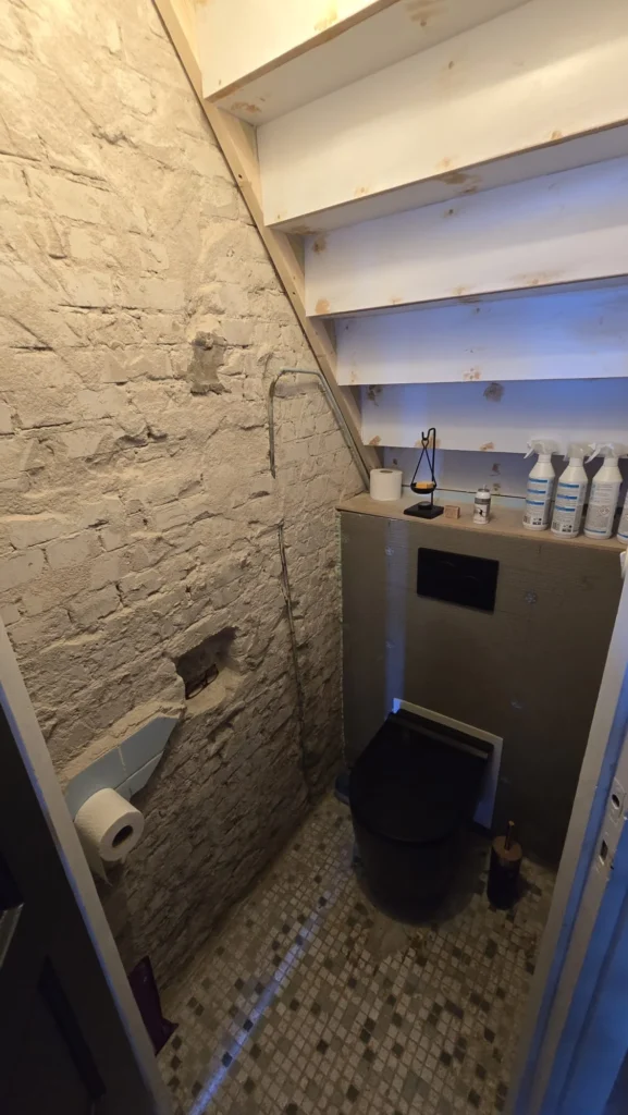 Compact toilet met zwarte wc, houten planken en steenlook wandafwerking